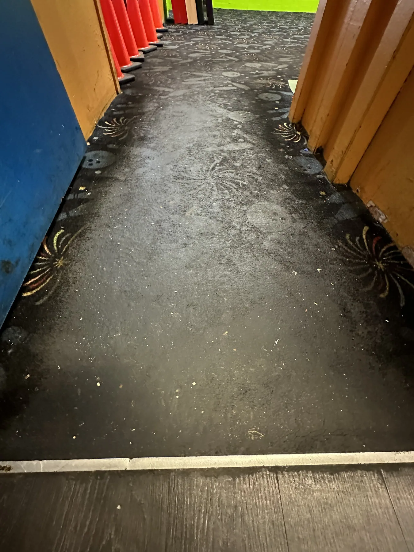 Heavily soiled bowling-themed commercial carpet in an entryway hallway before dry cleaning, dirt ground into the fireworks and bowling pin pattern